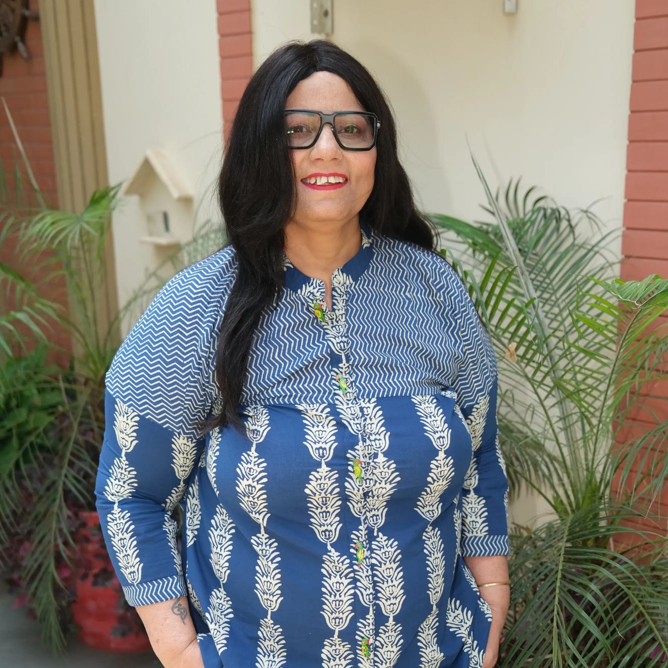 Woman with long black hair and glasses smiling in blue patterned top